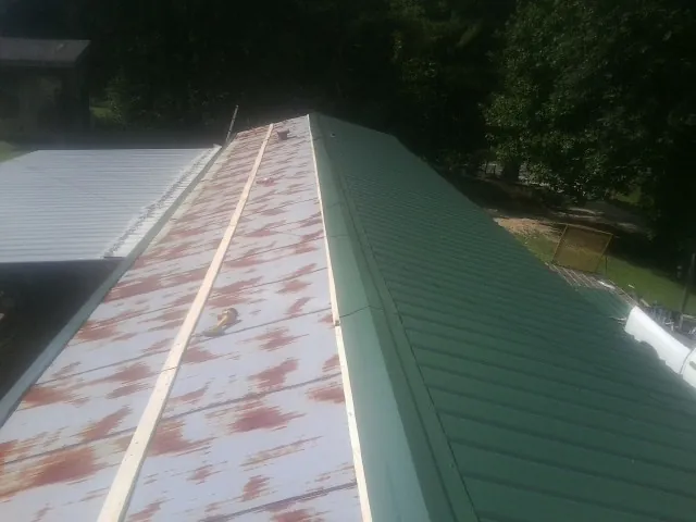 Old rusted panels beside newly installed green metal roofing — Wind Damage Roof Repair by Roofing Brothers in Wellersburg