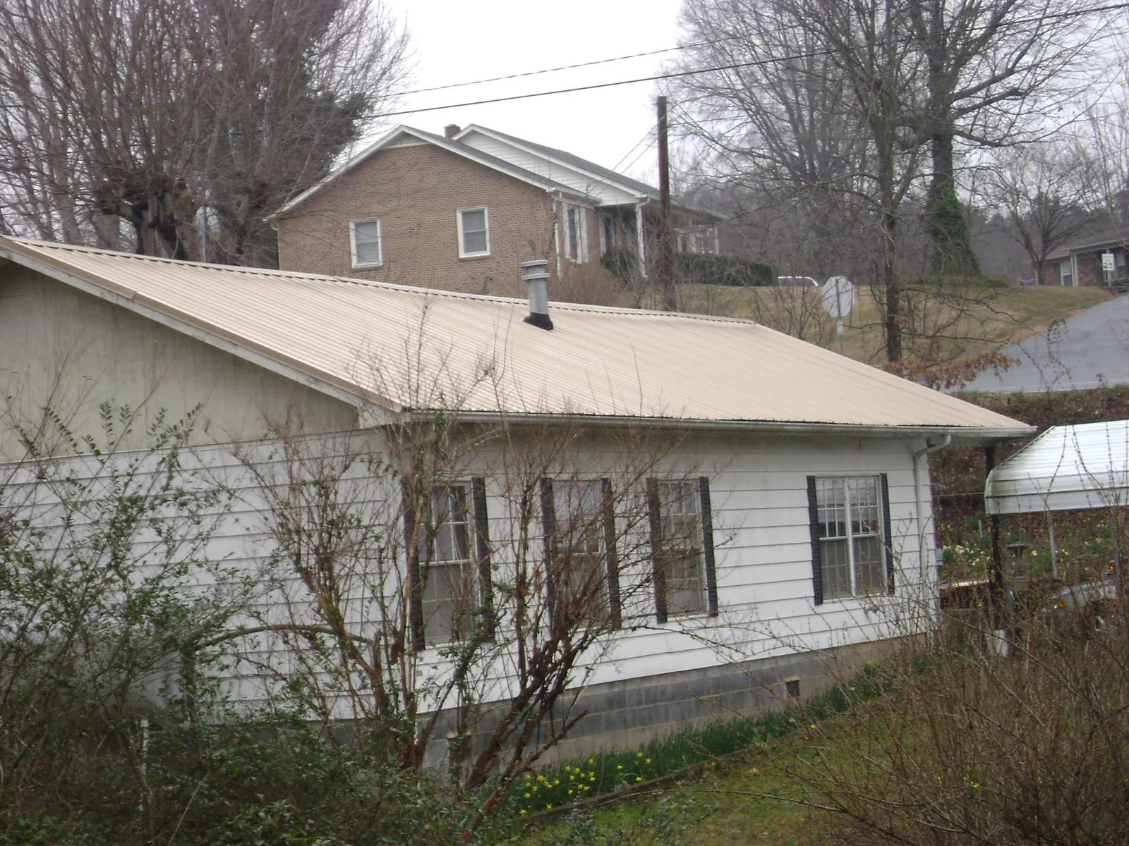 Tan metal roof on a white sided house set into a hillside — Commercial Roofing by Roofing Brothers in Wellersburg